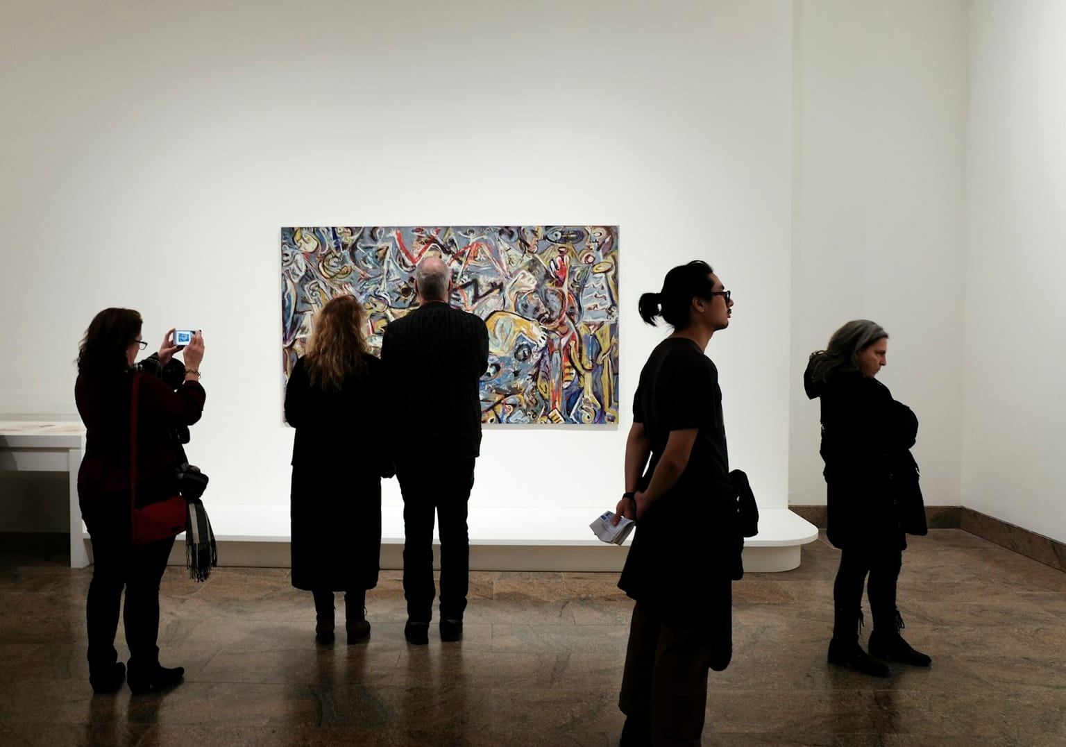People gathered in front of one bold, expressive painting in a gallery, drawn in close.
