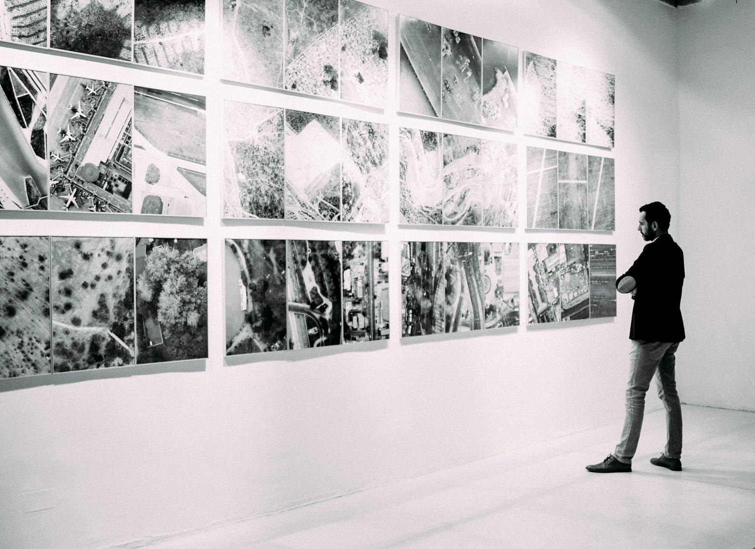 A monochrome grid of near-identical aerial photographs in a gallery — interchangeable units that blur into one.